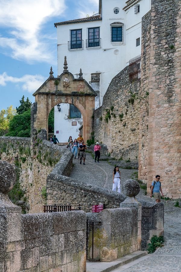 This may contain: people walking up and down an old cobblestone street in the city with stone walls