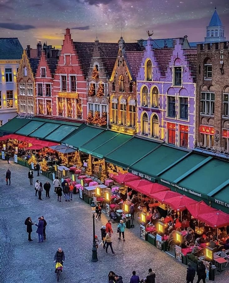 This may contain: people are walking around an outdoor market in the city at dusk, with red umbrellas and green awnings