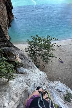 This may contain: a person is climbing up the side of a cliff by the beach with their feet in the air