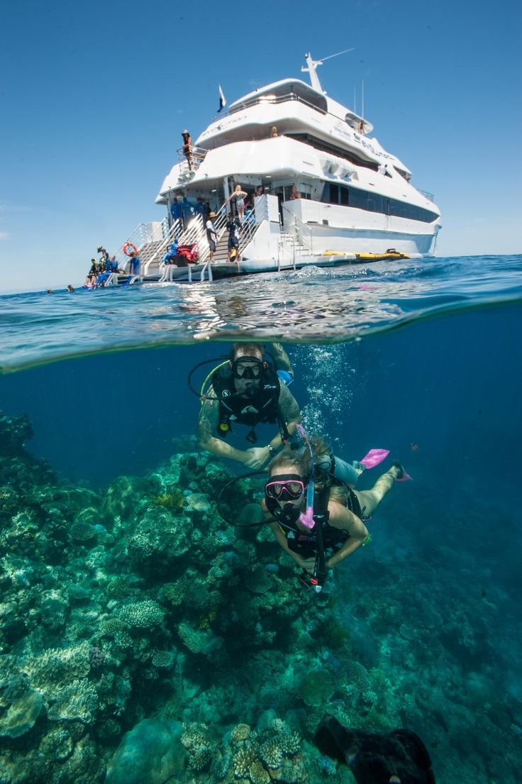 This may contain: two people diving in front of a large boat on the ocean with scuba gear and snorkels