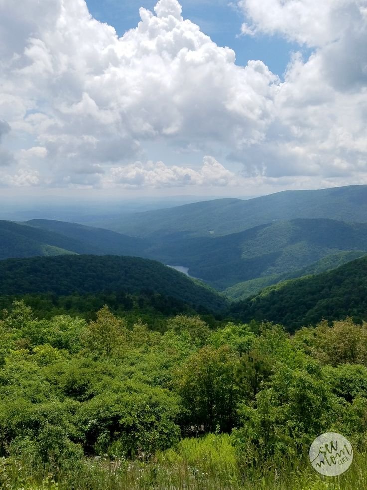 This may contain: a scenic view of mountains and trees from the top of a hill with clouds in the sky