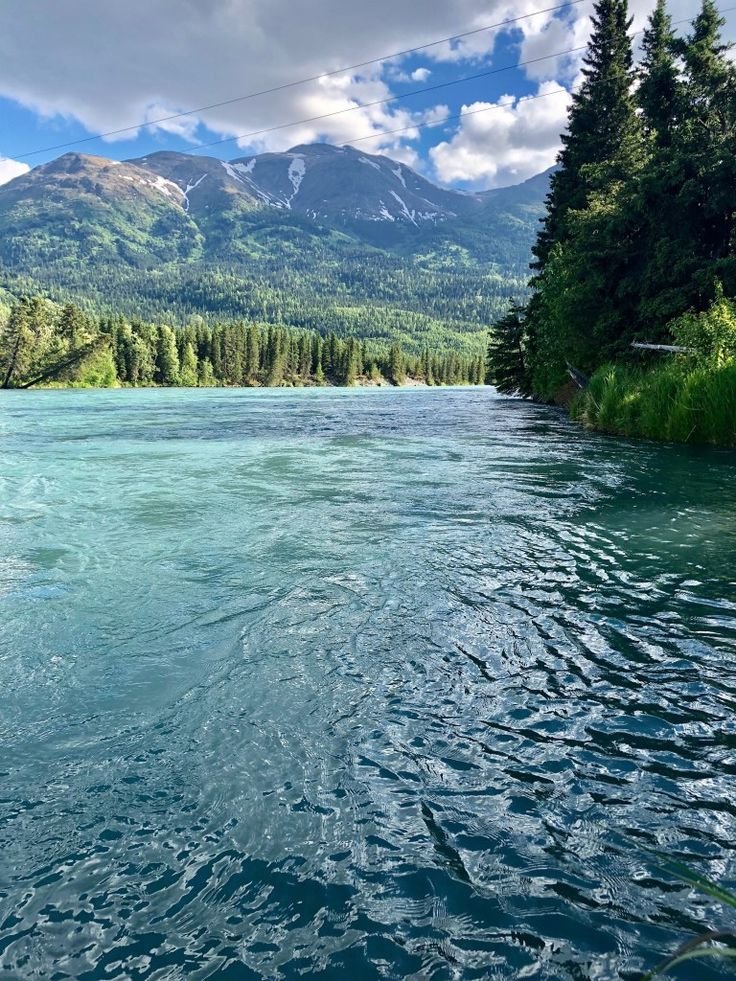 This may contain: the water is very blue and green with mountains in the background