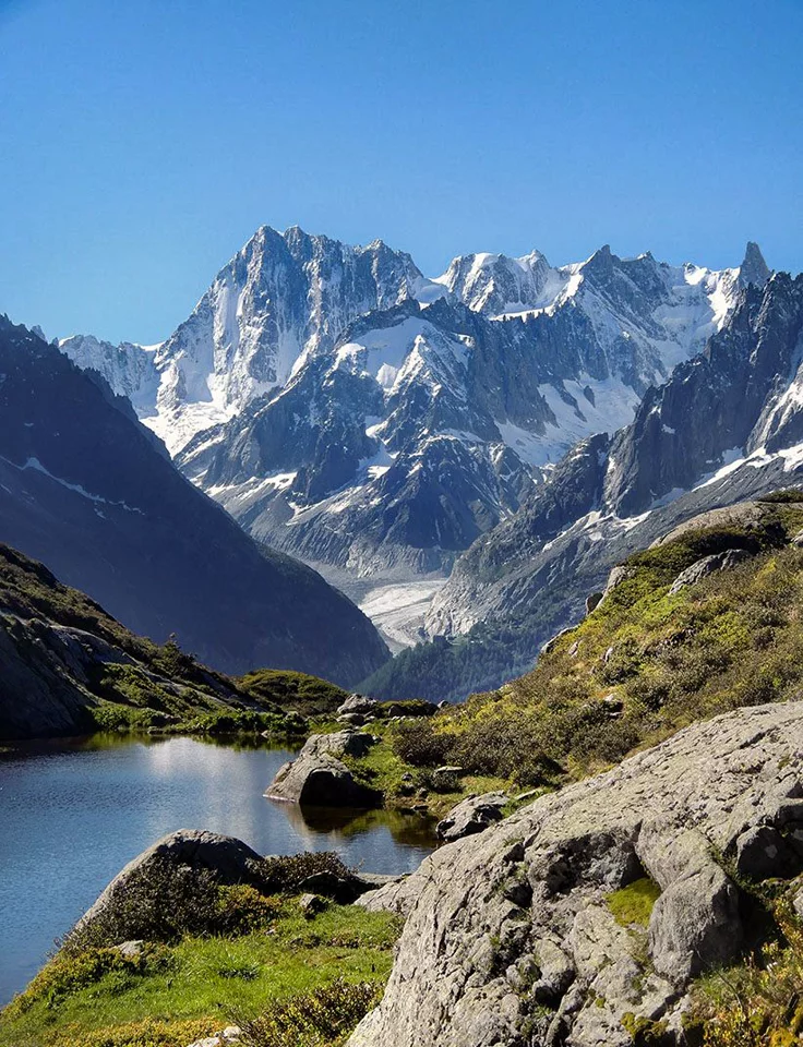 This may contain: the mountains are covered in snow and green grass near a body of water with rocks on both sides
