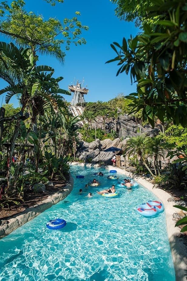 This may contain: people are swimming in an artificial pool surrounded by palm trees and water slides at universal studios