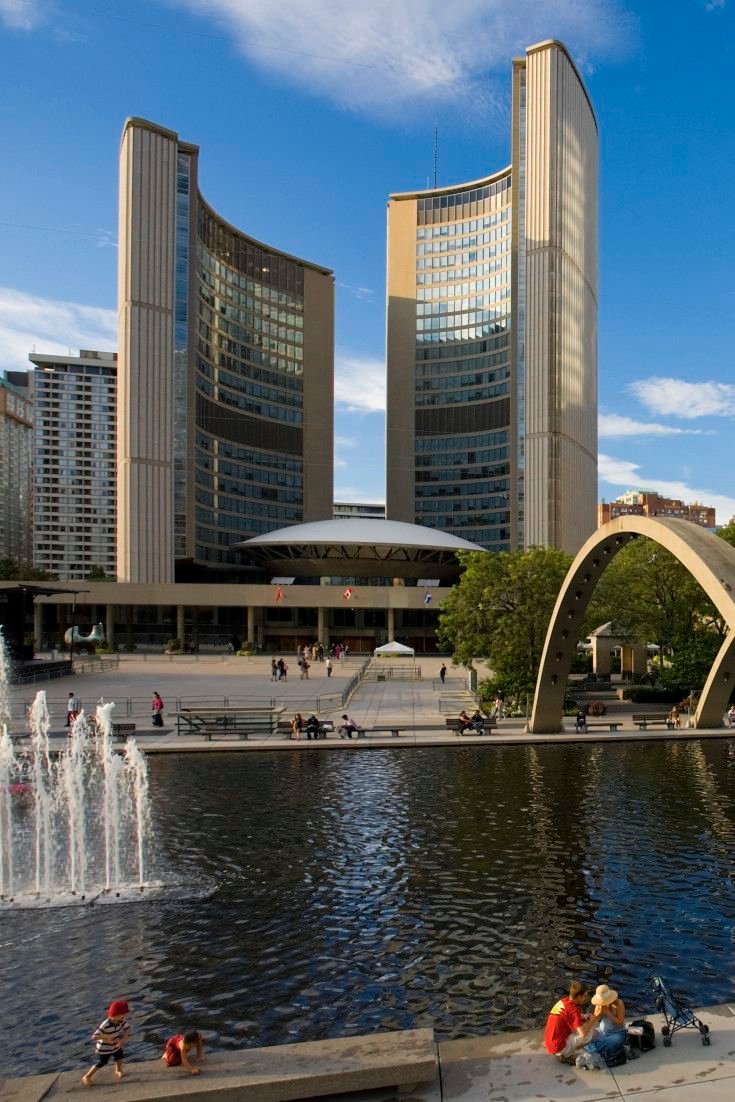 This may contain: people are sitting on the edge of a pond in front of some buildings and fountains