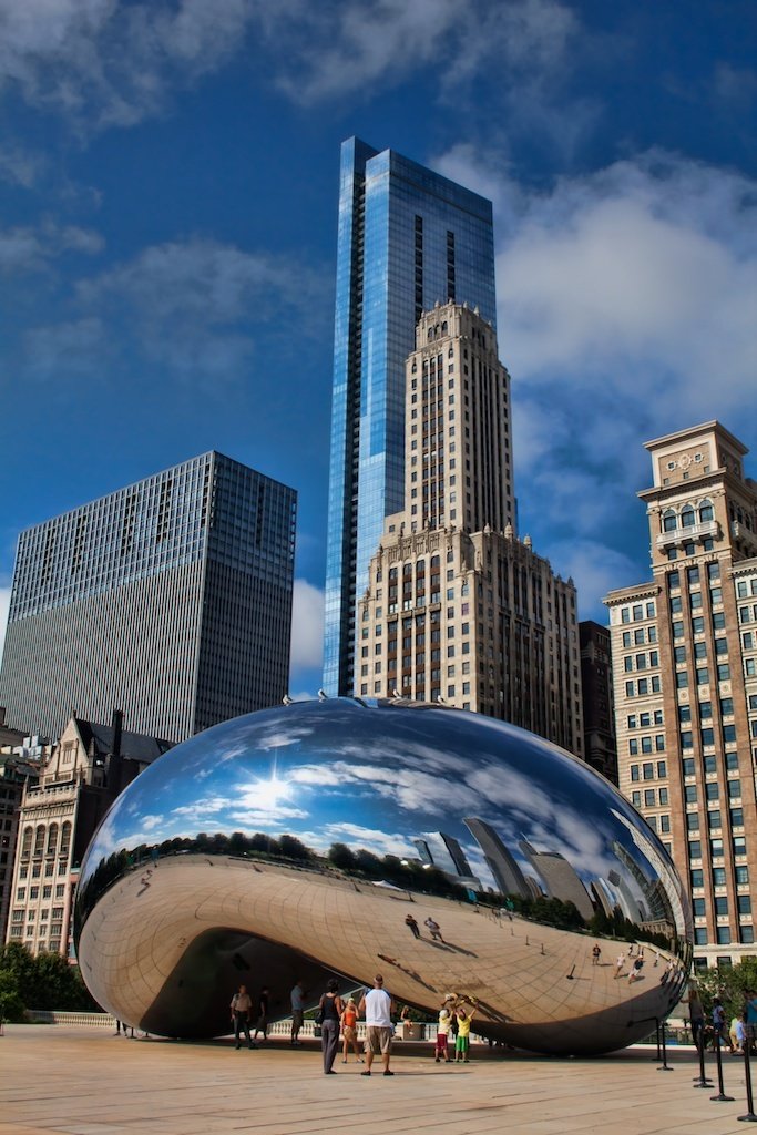 This may contain: people are standing in front of a large shiny object with skyscrapers in the background