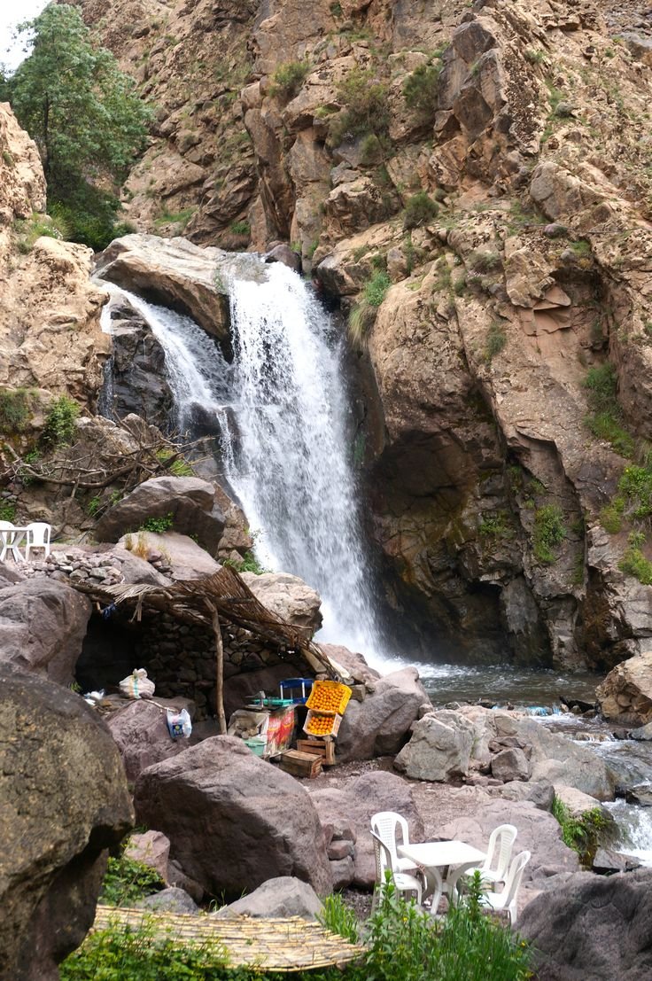 This may contain: there is a small waterfall in the middle of this rocky area with people sitting at tables under it