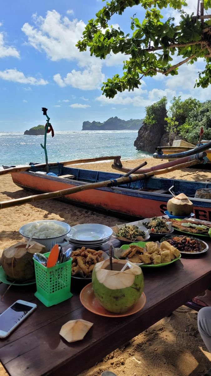 This may contain: a wooden table topped with plates of food next to the ocean and boats in the background