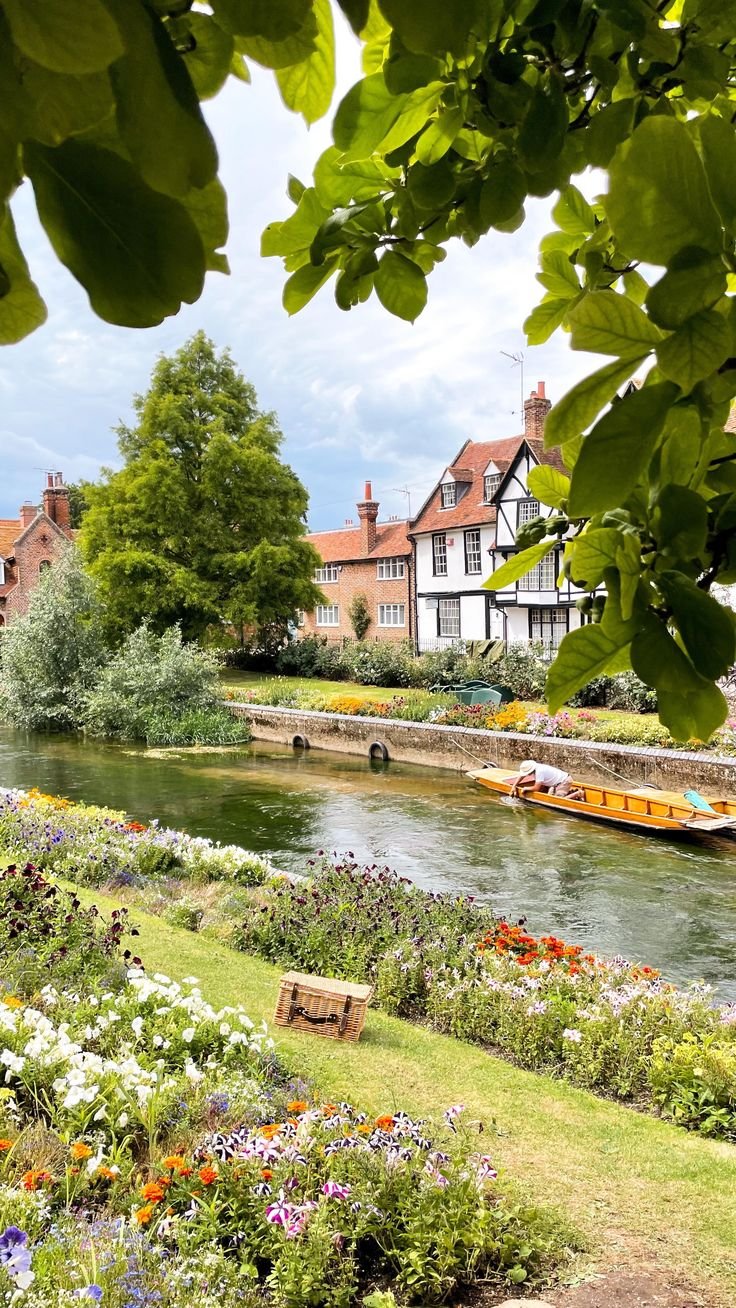 This may contain: there is a boat that is going down the river in front of houses and flowers