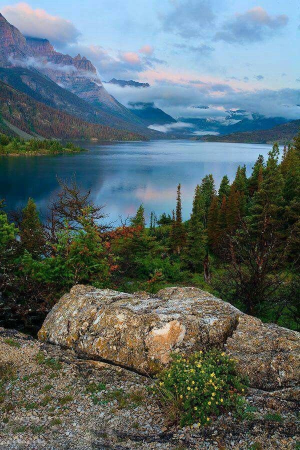 This may contain: a large rock sitting on top of a lush green hillside next to a body of water