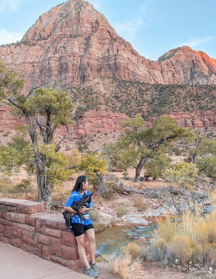 This may contain: a woman standing on a wall next to a river and mountains in the back ground