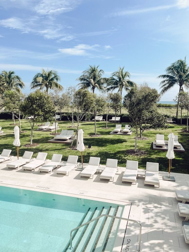This may contain: an empty swimming pool surrounded by lawn chairs and palm trees
