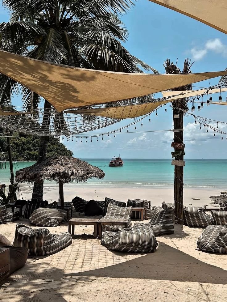 This may contain: an outdoor seating area with umbrellas and chairs on the beach