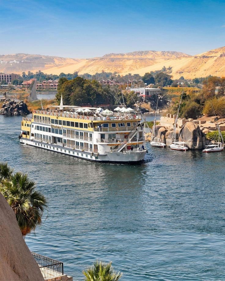 This may contain: a large white boat floating on top of a river next to a rocky cliff covered hillside