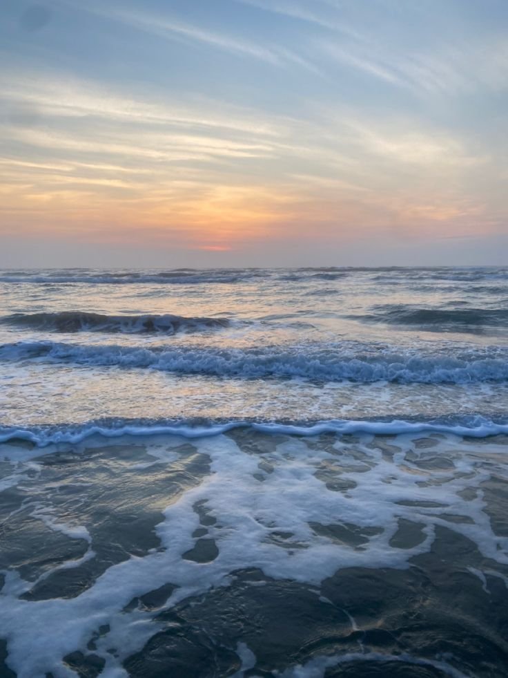 This may contain: the sun is setting over the ocean with waves coming in to shore and some clouds