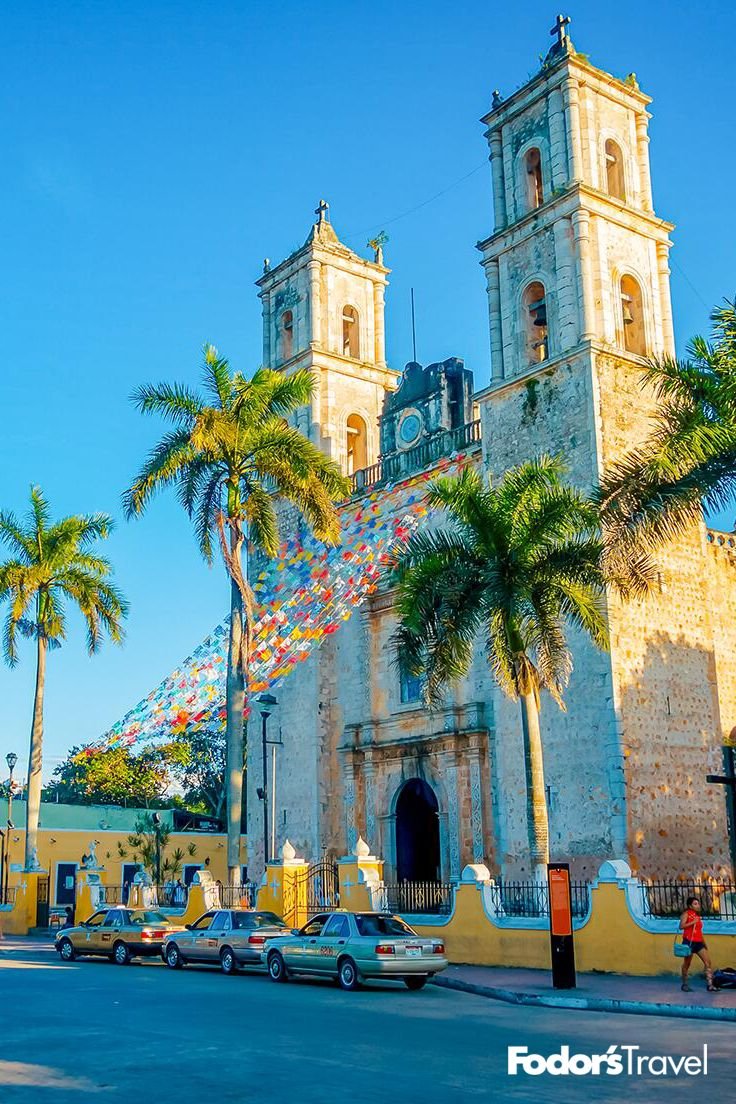 This may contain: cars parked in front of an old church with flags flying from it's towers
