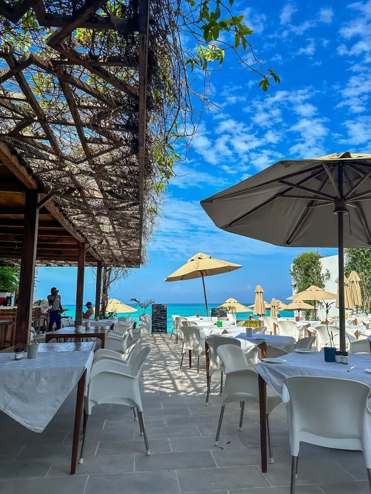 This may contain: tables and chairs with umbrellas are set up for an outdoor dining area on the beach