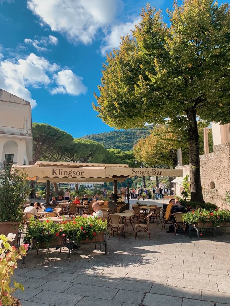 This may contain: people are sitting at tables under umbrellas on a sunny day in the town square