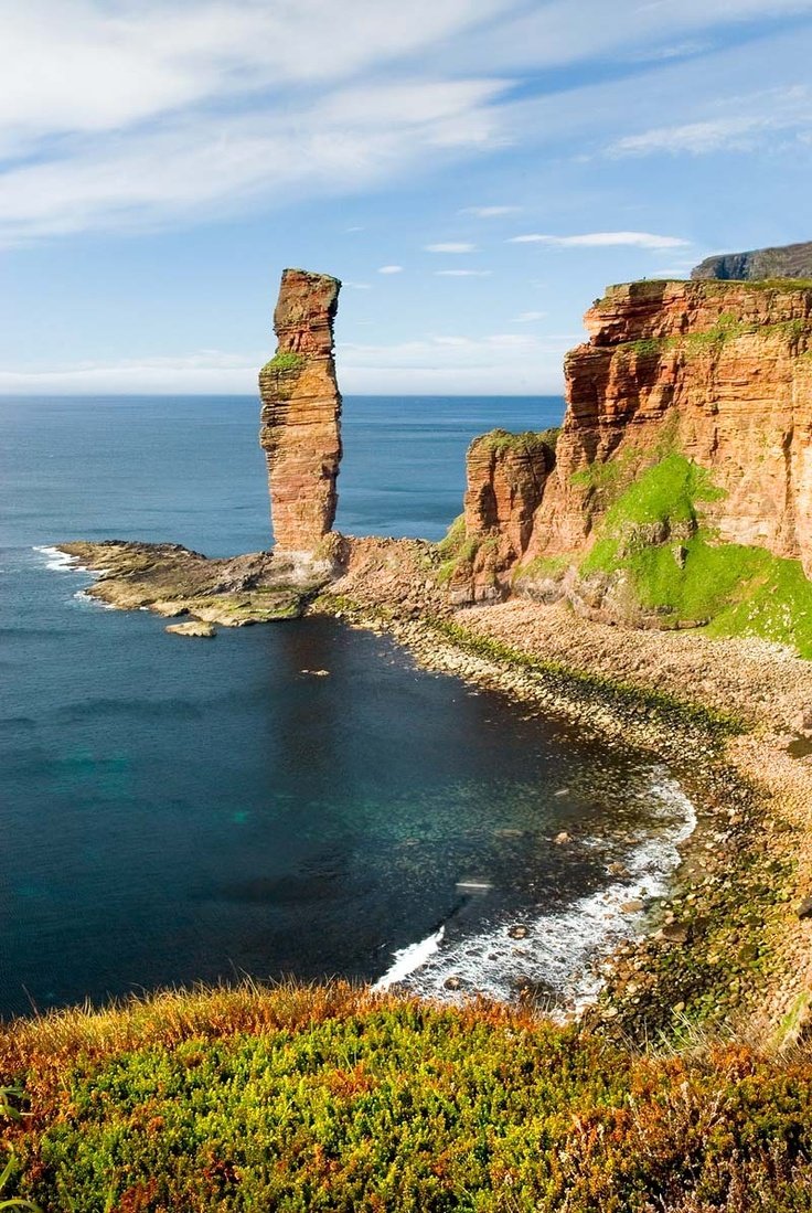 This may contain: an ocean cliff with two tall rocks sticking out of it's sides next to the water