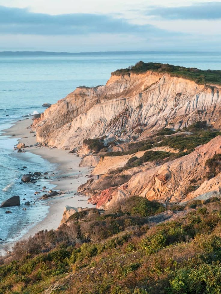 This may contain: the ocean is next to a rocky cliff with white and brown cliffs on it's sides