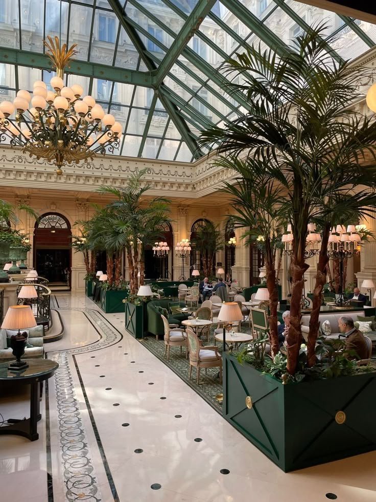 This may contain: the inside of a hotel lobby with palm trees and chandeliers hanging from the ceiling