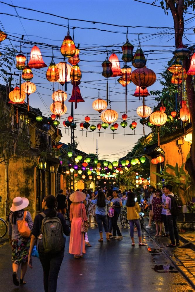 This may contain: many people are walking down the street with lanterns hanging from the wires above them at night