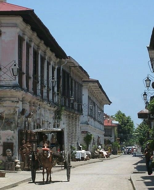 This may contain: a horse and buggy traveling down a street in front of old buildings with balconies