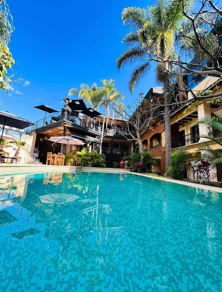 This may contain: an outdoor swimming pool with lounge chairs and umbrellas next to the resort's main building