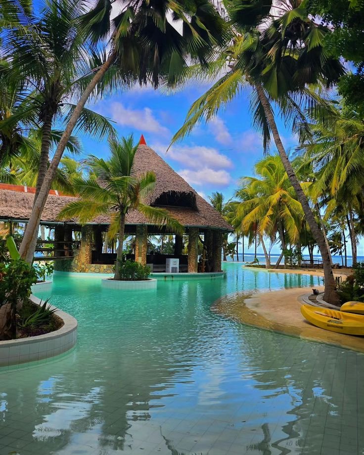This may contain: an outdoor swimming pool surrounded by palm trees and water features a gazebo with thatched roof