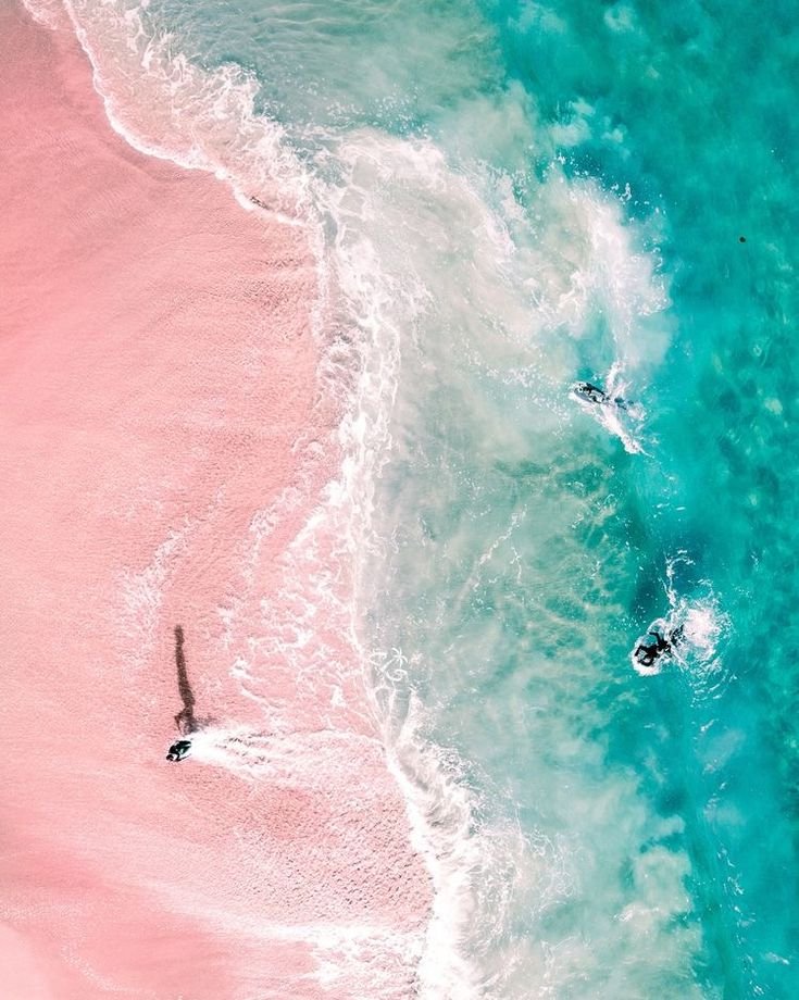 This may contain: two people are swimming in the ocean with pink sand and clear blue water as seen from above