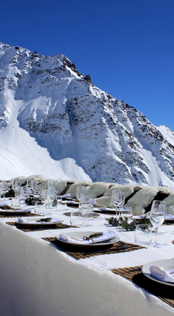 This may contain: the table is set with white plates and silverware in front of a snowy mountain