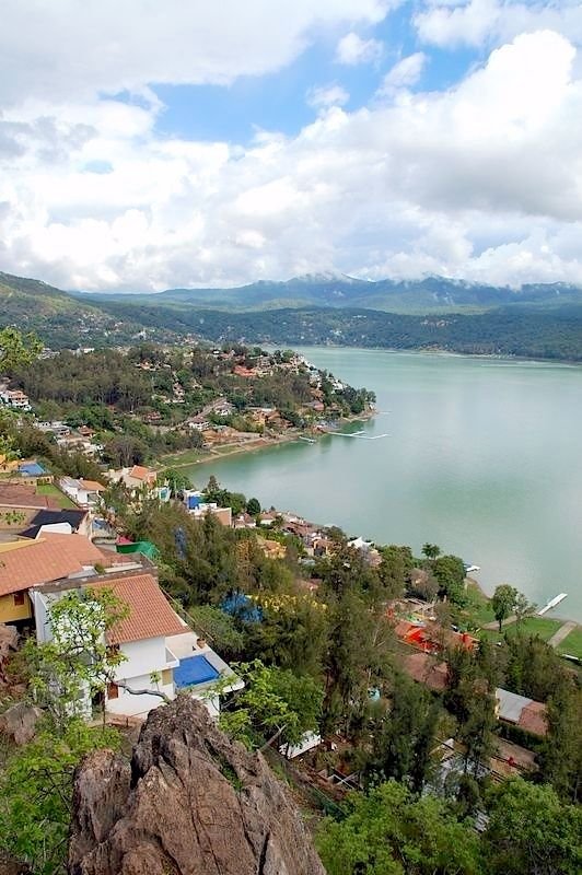 This may contain: an aerial view of a lake surrounded by trees and buildings with mountains in the background