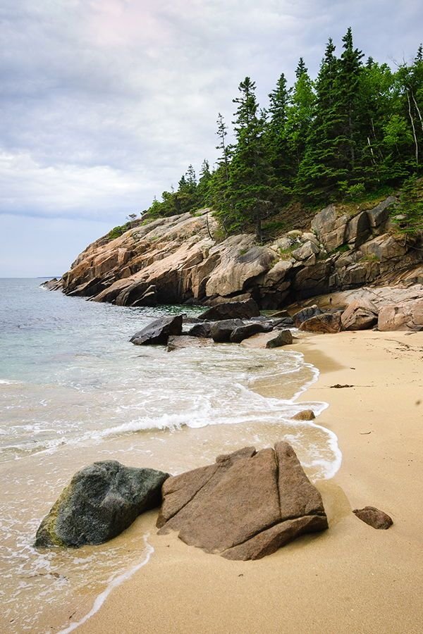 This may contain: a beach with large rocks and trees on the shore