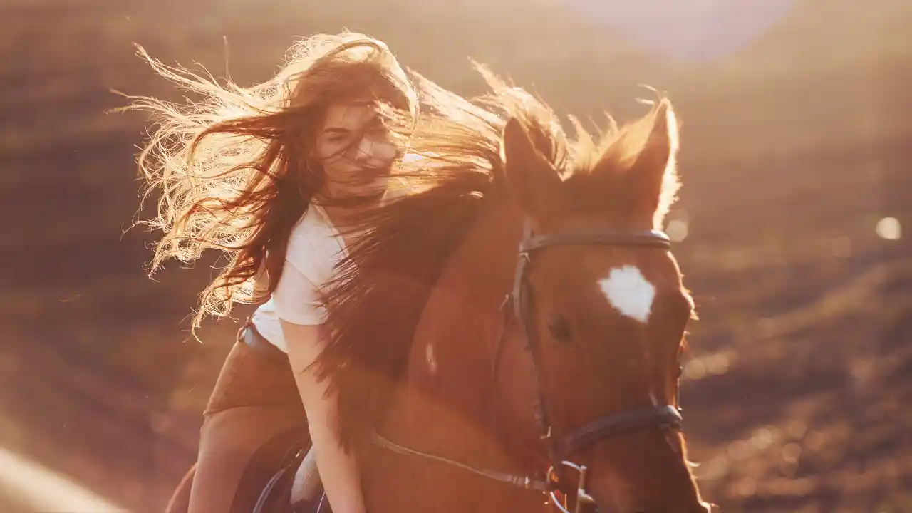 Young woman in protective hat with horse in sunny agricultural field, celebrating National Ride Your Horse to a Bar Day.