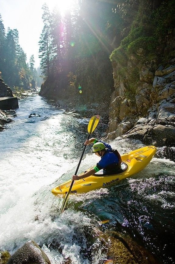 This may contain: a man is kayaking down a river in the sun with rocks and trees around him