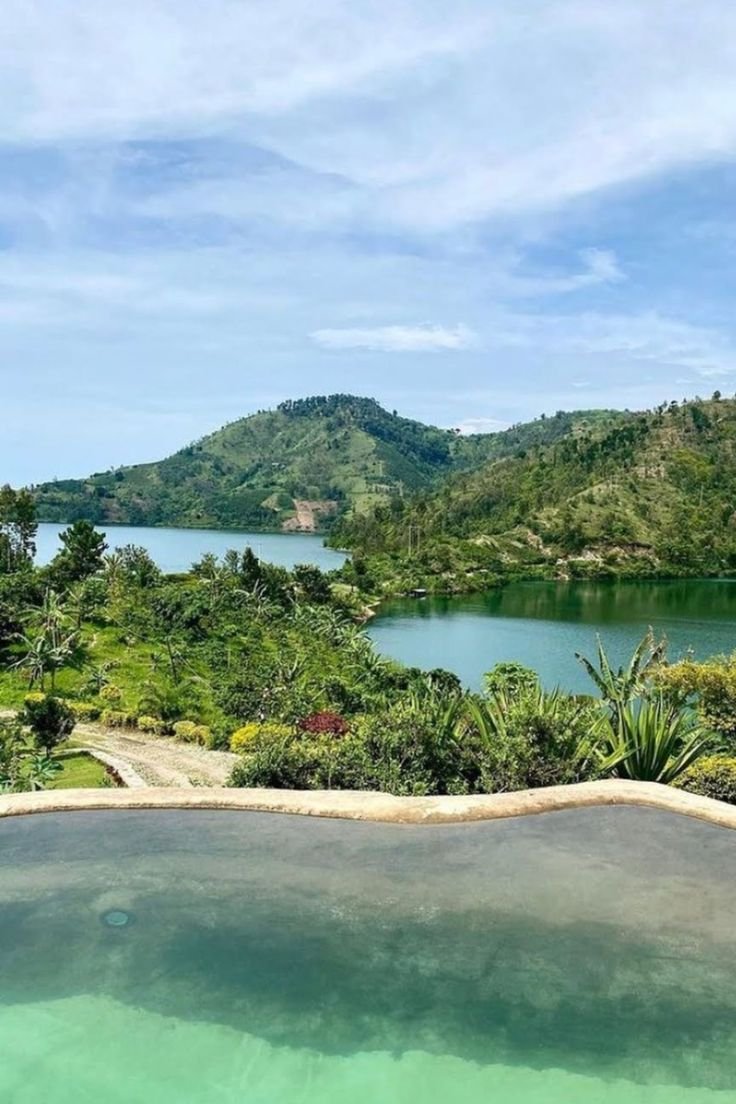 This may contain: an outdoor swimming pool surrounded by lush green trees and mountains in the distance with blue sky
