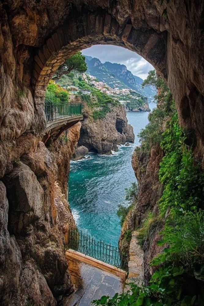 This may contain: an arch in the side of a cliff with water below