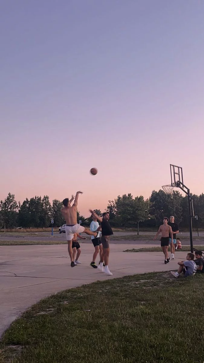 This may contain: some people are playing basketball on a court at sunset or dawn with the sun going down