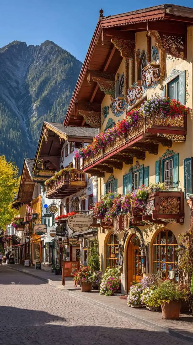 This may contain: an old european town with flowers on the balconies and mountains in the background