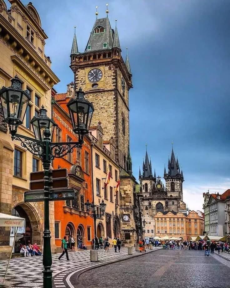 This may contain: a clock tower towering over a city filled with tall buildings and people walking down the street