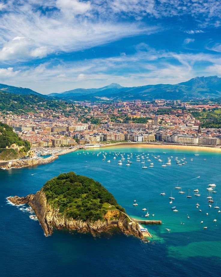 This may contain: an island in the middle of water with boats floating on it's sides and mountains in the background