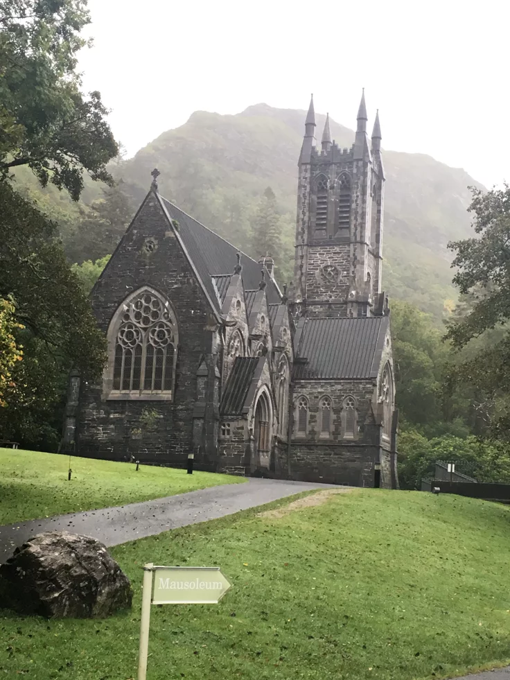 This may contain: an old church sits in the middle of a grassy area with trees and mountains behind it