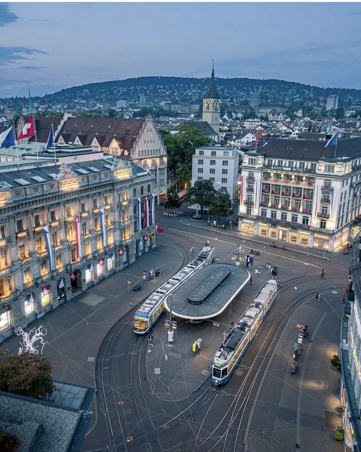 This may contain: an aerial view of a city with buses and buildings in the foreground, at dusk