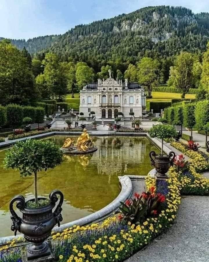 This may contain: a large white house sitting next to a lush green forest filled with trees and flowers