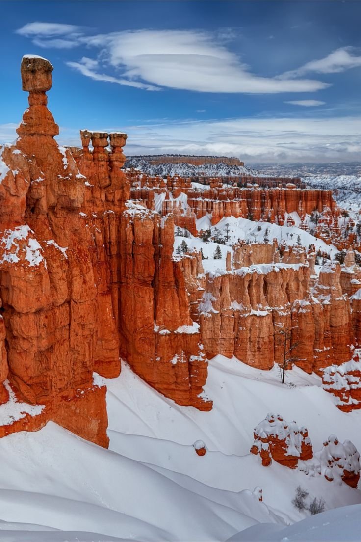 This may contain: snow covers the ground in front of large rock formations