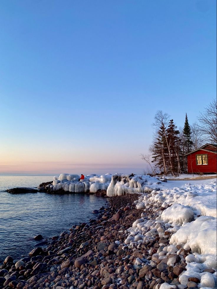 This may contain: a red house sitting on top of a snow covered shore