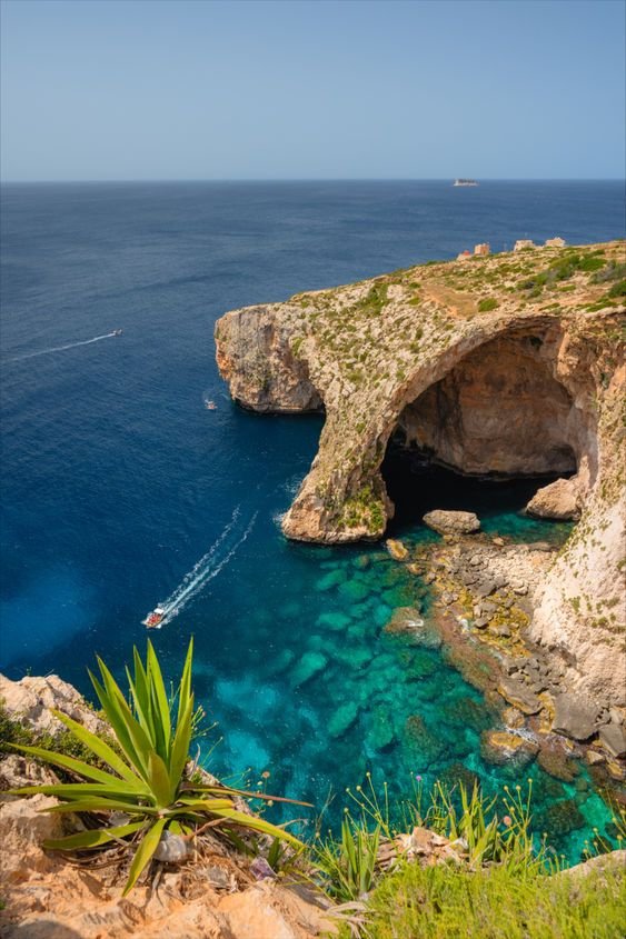 This may contain: the water is crystal blue and there are boats in the ocean near an arch shaped rock formation