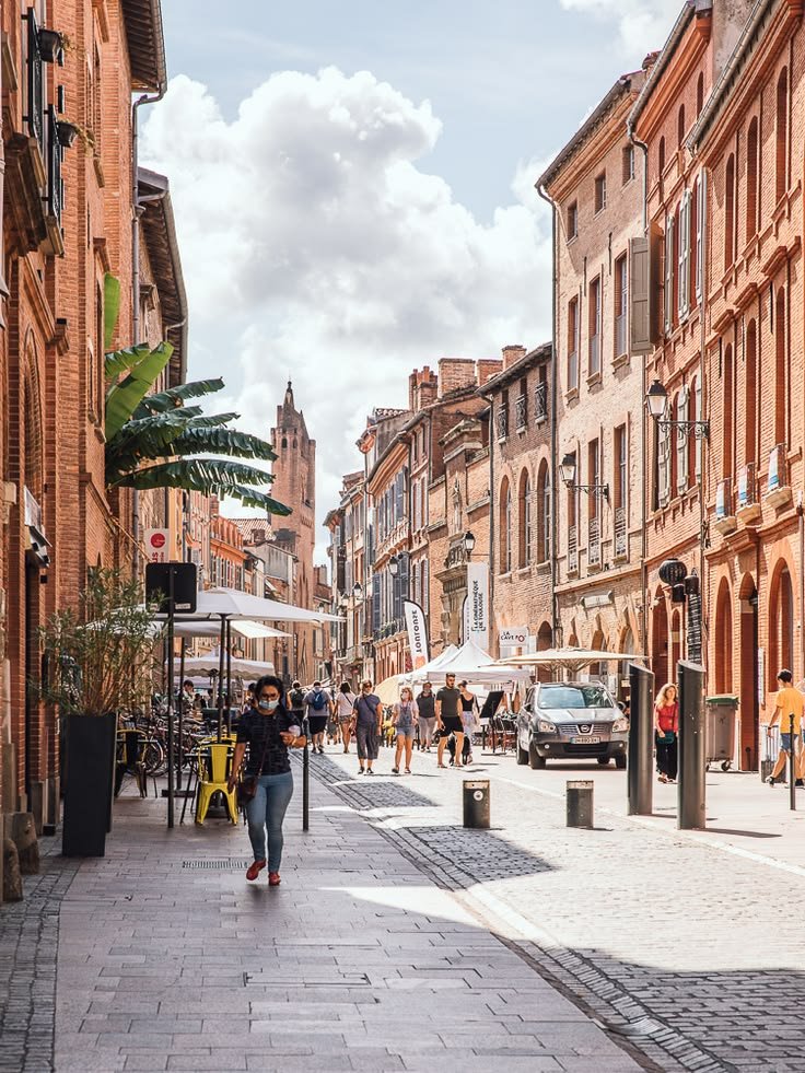 This may contain: people are walking down the street in an old town with brick buildings and shops on both sides