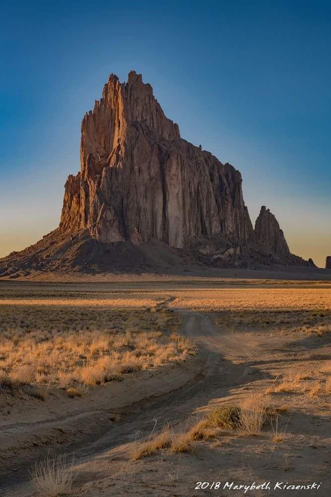 This may contain: a large rock formation in the middle of a desert with dirt roads and grass on both sides