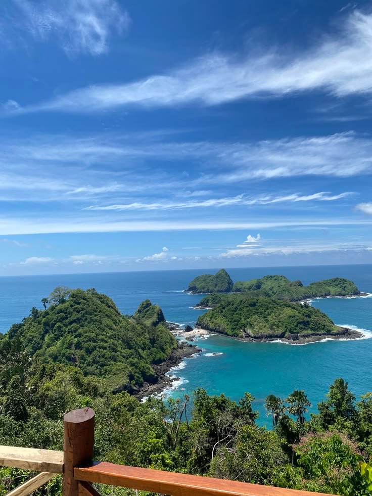 This may contain: a wooden bench sitting on top of a lush green hillside next to the ocean with small islands in the distance